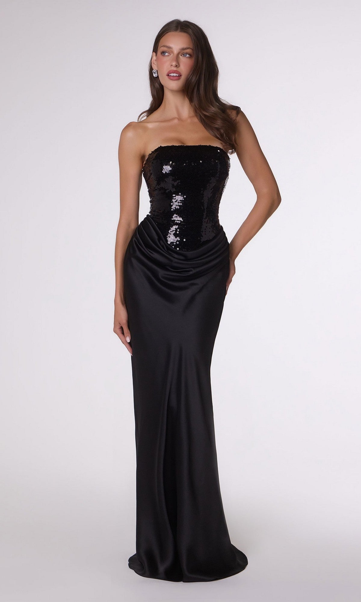 A woman wearing the Long Prom Dress: Amoris T744 in black, which features a stunning sequin bodice and a smooth, draped satin skirt that falls gracefully to the floor, stands against a plain light background.